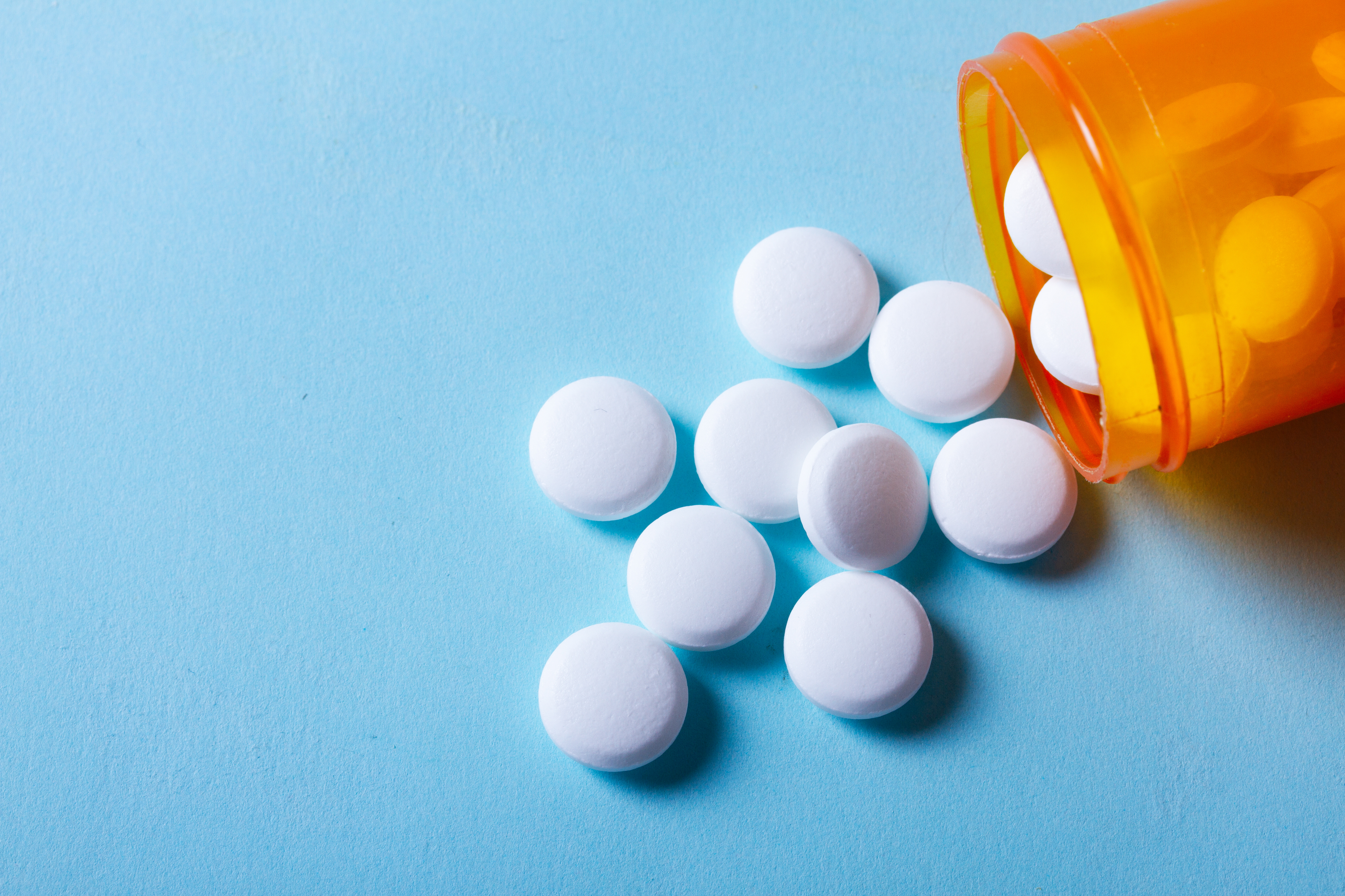 Pills spilling out of bottle onto blue background